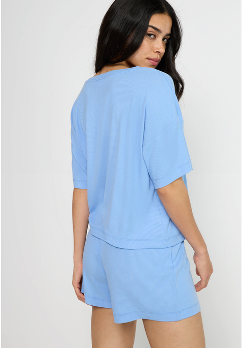 Bild: Shorty von LSCN by LASCANA: Lässiger Look, maximaler Komfort: Der Shorty von LSCN by Lascana bringt dich in den perfekten Chill-Modus. Das kurze, leger geschnittene Halbarmshirt mit überschnittenen Schultern bietet dir eine entspannte Passform, die dich nicht nur nachts, sondern auch beim Relaxen zu Hause begleitet. Die Shorts mit geradem Bein und einer kurzen Zier-Knopfleiste setzen ein süßes Detail und sorgen für einen coolen Look. Die weiche, elastische Rippqualität fühlt sich richtig angenehm auf der Haut an. Dadurch ist der Pyjama perfekt für gemütliche Abende. Kuschel dich ein und genieße den Komfort – mit dem Shorty von LSCN by Lascana.