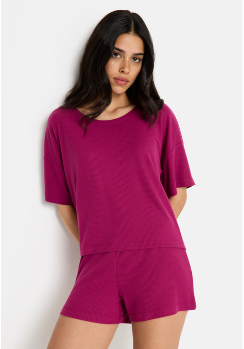 Bild: Shorty von LSCN by LASCANA: Lässiger Look, maximaler Komfort: Der Shorty von LSCN by Lascana bringt dich in den perfekten Chill-Modus. Das kurze, leger geschnittene Halbarmshirt mit überschnittenen Schultern bietet dir eine entspannte Passform, die dich nicht nur nachts, sondern auch beim Relaxen zu Hause begleitet. Die Shorts mit geradem Bein und einer kurzen Zier-Knopfleiste setzen ein süßes Detail und sorgen für einen coolen Look. Die weiche, elastische Rippqualität fühlt sich richtig angenehm auf der Haut an. Dadurch ist der Pyjama perfekt für gemütliche Abende. Kuschel dich ein und genieße den Komfort – mit dem Shorty von LSCN by Lascana.